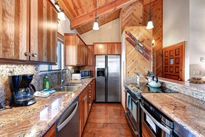A kitchen with wooden cabinets, stainless steel appliances, granite countertops, and a herringbone-patterned wall. - Ski in/Ski out- Timber Ridge 28 (Mammoth Lakes)