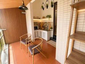 Een moderne keuken met witte kasten, een magnetron en een spoelbak. Er staan twee houten stoelen met kussens.