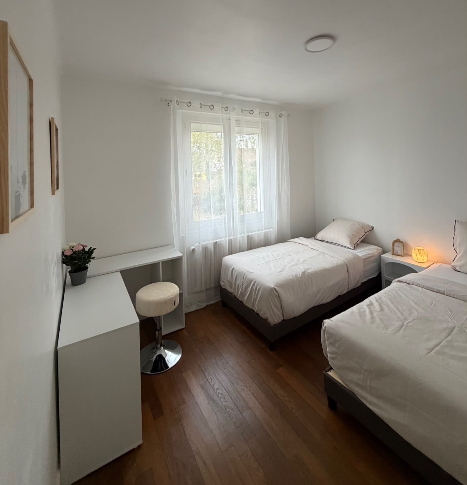 A bedroom with two beds, a desk, a chair, and a window with curtains.