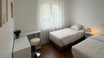 Un dormitorio con dos camas, un escritorio, una silla y una ventana con cortinas.