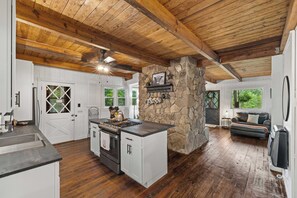 A spacious kitchen with a stone accent wall, wooden ceiling beams, and a large island stove. - Pond in the Pines | Aska Farm Stay + Fishing (Blue Ridge)