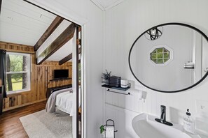 A bathroom with a white sink, a round mirror, and a toilet. - Pond in the Pines | Aska Farm Stay + Fishing (Blue Ridge)