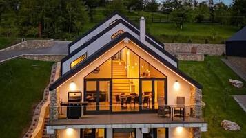 Une maison moderne à deux étages, dotée d’un balcon, de grandes fenêtres et d’une façade en pierre.
