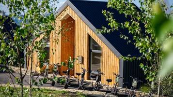 Een modern houten gebouw met een schuin dak, omringd door groen en fietsen.
