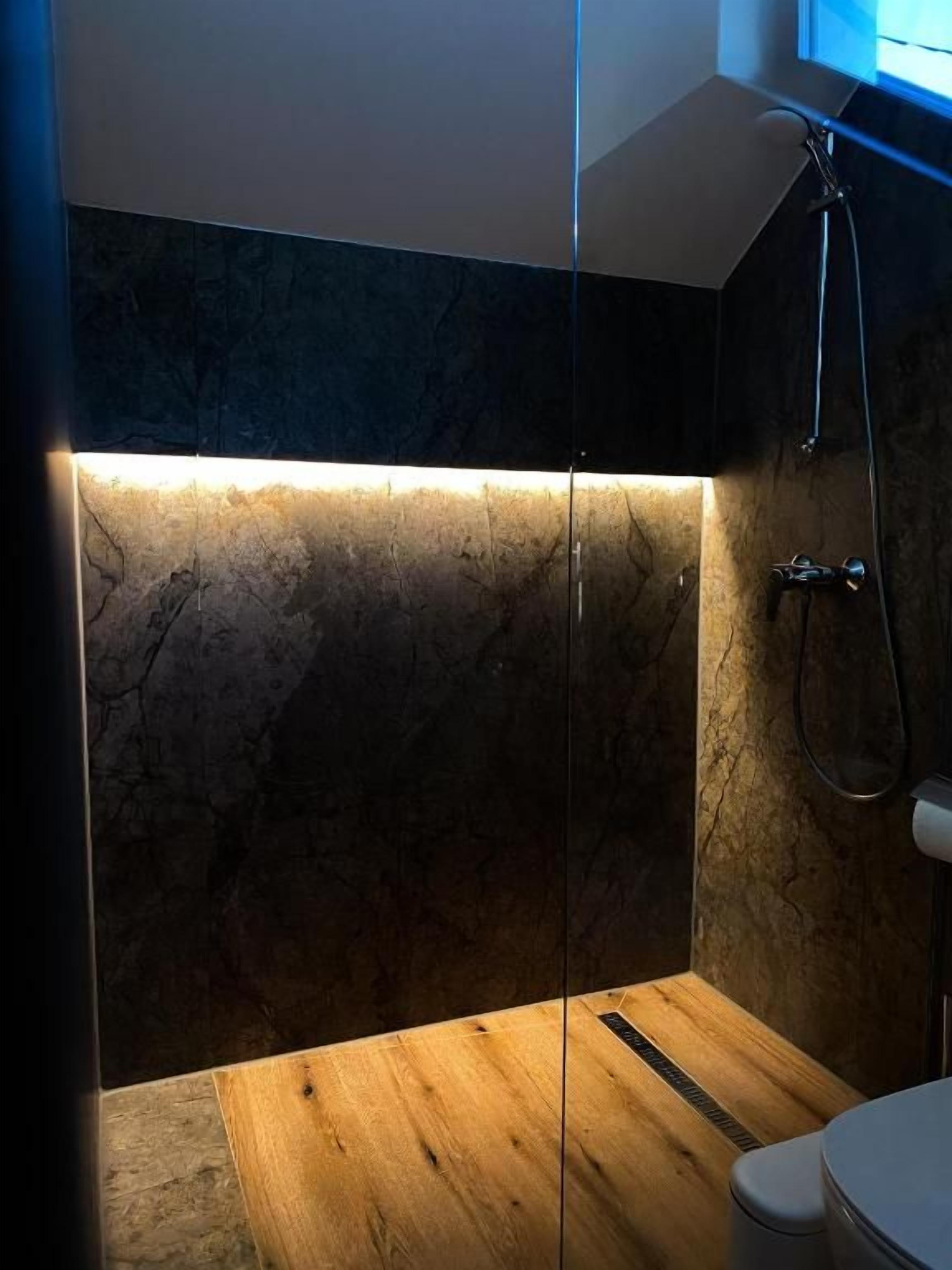 A modern bathroom with a glass shower enclosure, a wooden vanity, and a marble wall.