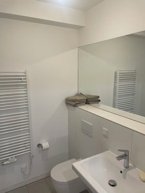 Ein modernes Badezimmer mit Toilette, Waschbecken, Spiegel, Handtuchhalter und einem an der Wand abgelegten Handtuch.
