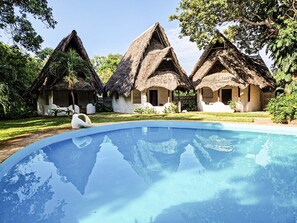 Ein Pool mit Reetdachhäusern im Hintergrund.