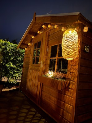 A wooden cabin with a large window, a hanging light fixture, and a small garden area. - Chalet Lebensfreude – A Getaway by the Water (Lathum)
