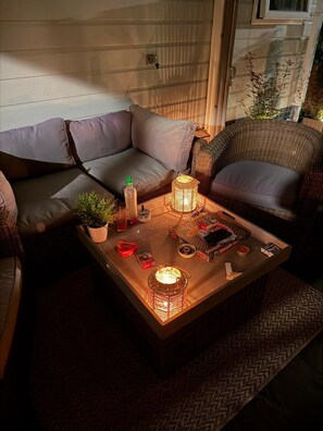 A cozy seating area with a cushioned sofa, wicker chairs, and a coffee table with decorative items and candles. - Chalet Lebensfreude – A Getaway by the Water (Lathum)
