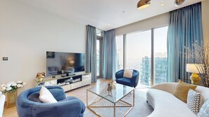 Ein modernes Wohnzimmer mit einem Flachbildfernseher, zwei Sofas, einem Couchtisch und einem großen Fenster mit Vorhängen.