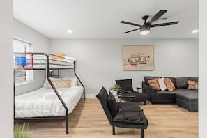 Ein modernes Wohnzimmer mit einem Etagenbett, einem schwarzen Ledersofa, einem kleinen Tisch mit einer Pflanze und einem Deckenventilator.