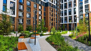 A modern multi-story residential building with a brick facade, large windows, and a landscaped courtyard with benches and pathways.