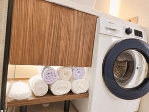 Una lavadora digital Samsung Inverter con un estante de madera debajo donde se guardan toallas dobladas con cuidado.