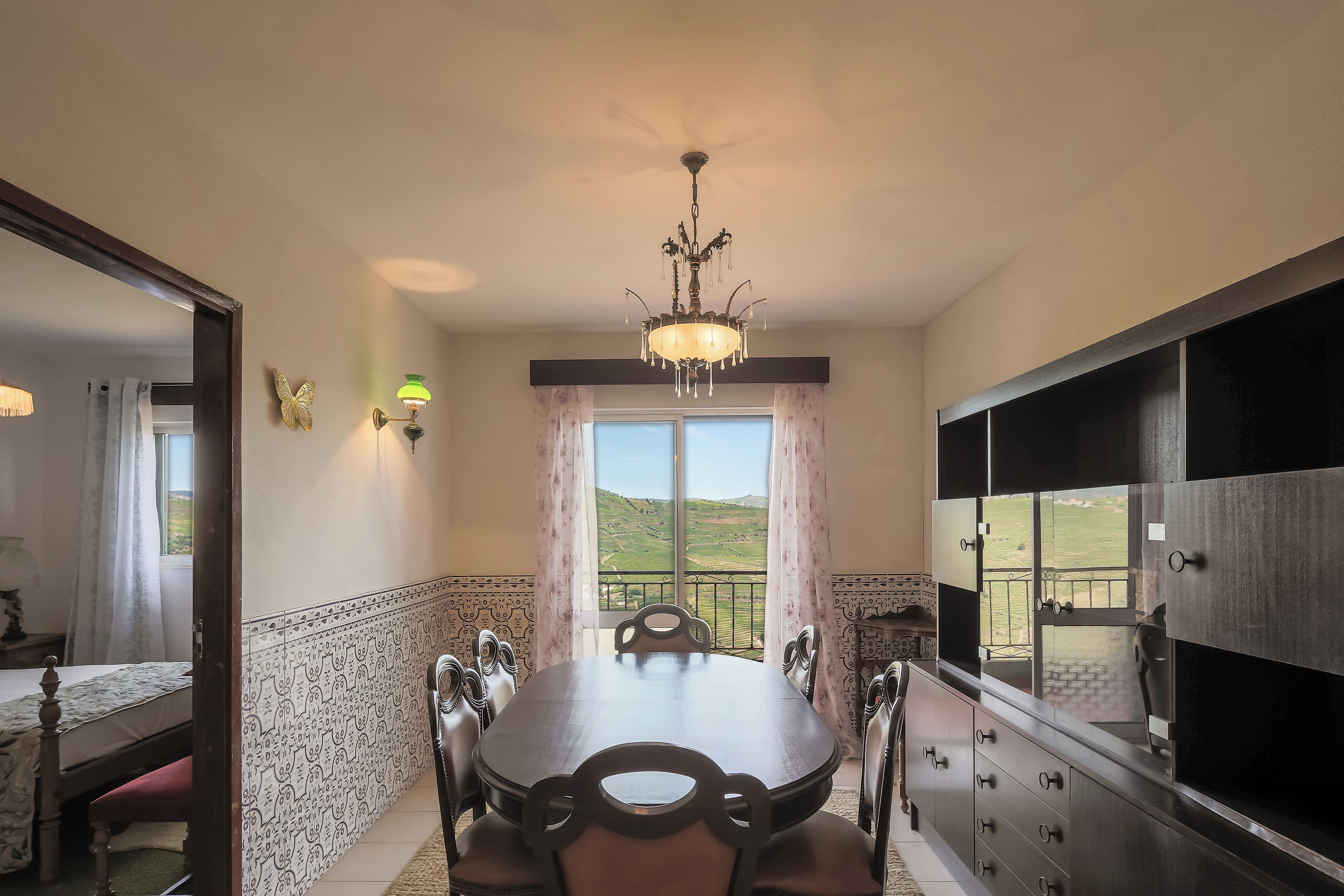 A dining room with a chandelier, a view of the countryside, and a large cabinet with drawers.