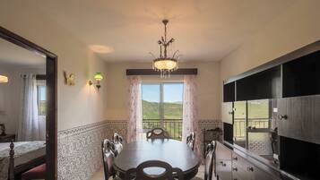 A dining room with a chandelier, a view of the countryside, and a large cabinet with drawers.