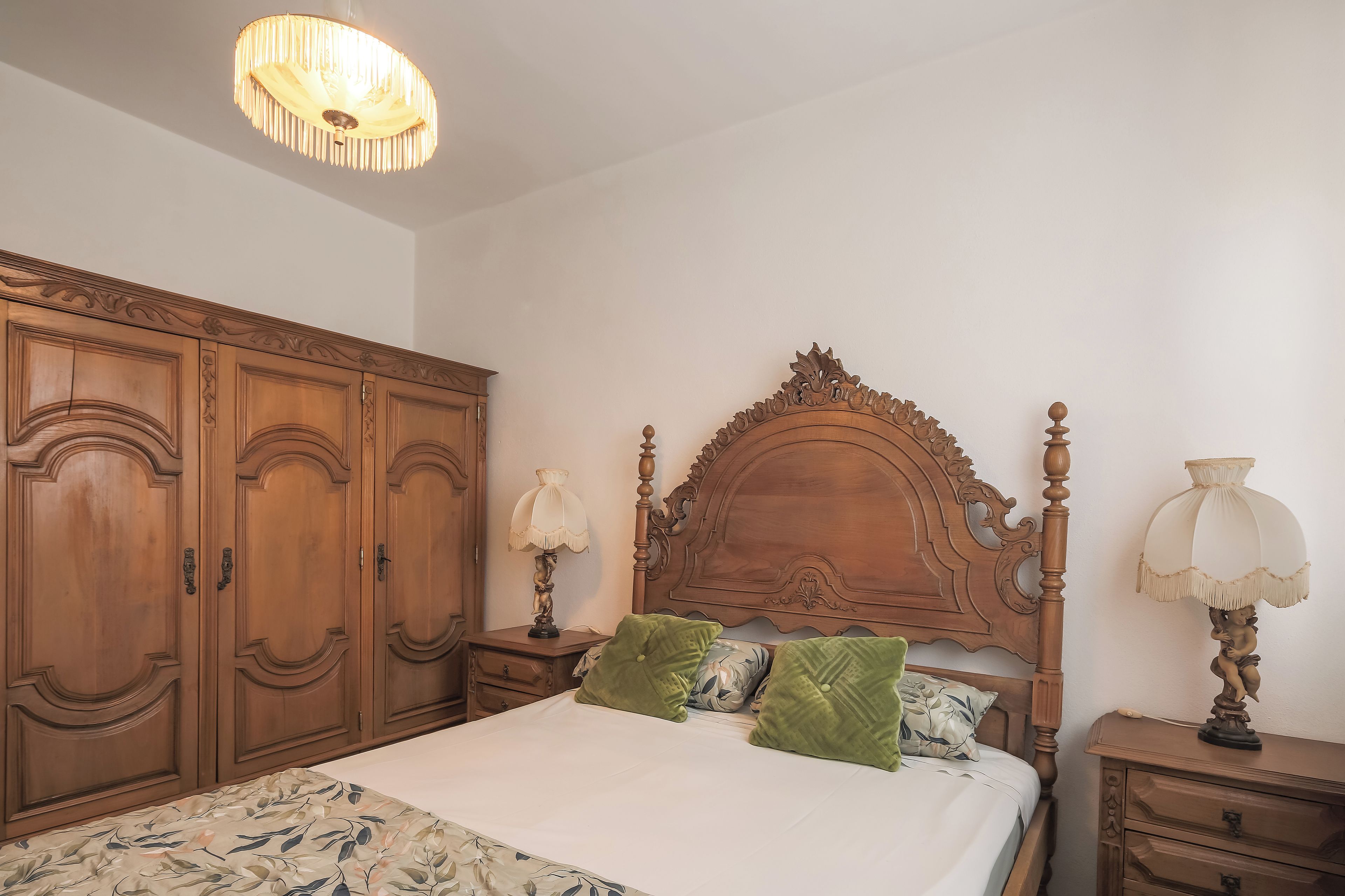 A bedroom with a wooden bed, a nightstand, a lamp, and a wardrobe.