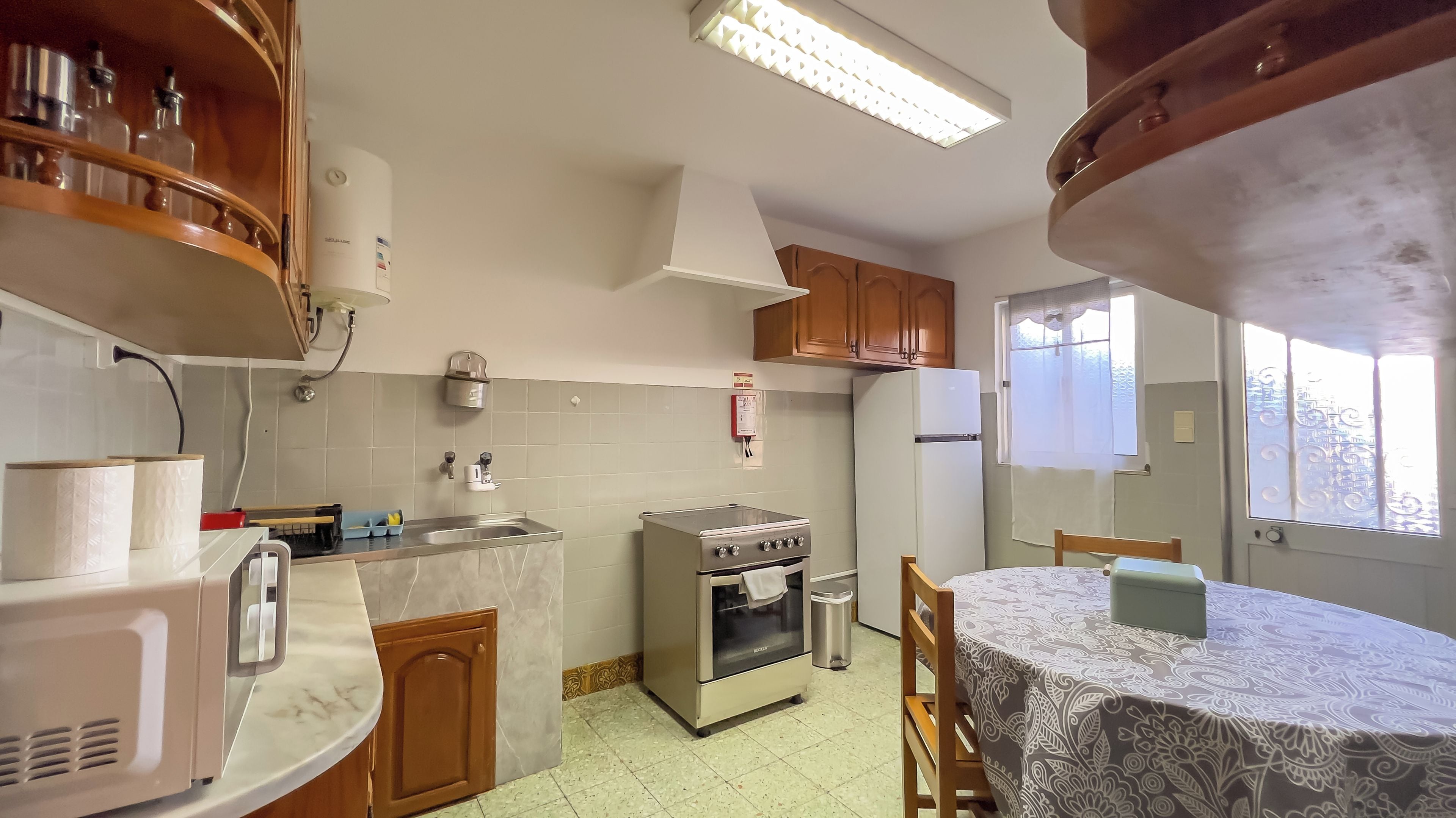 A kitchen with a refrigerator, stove, microwave, and a dining table with a tablecloth.