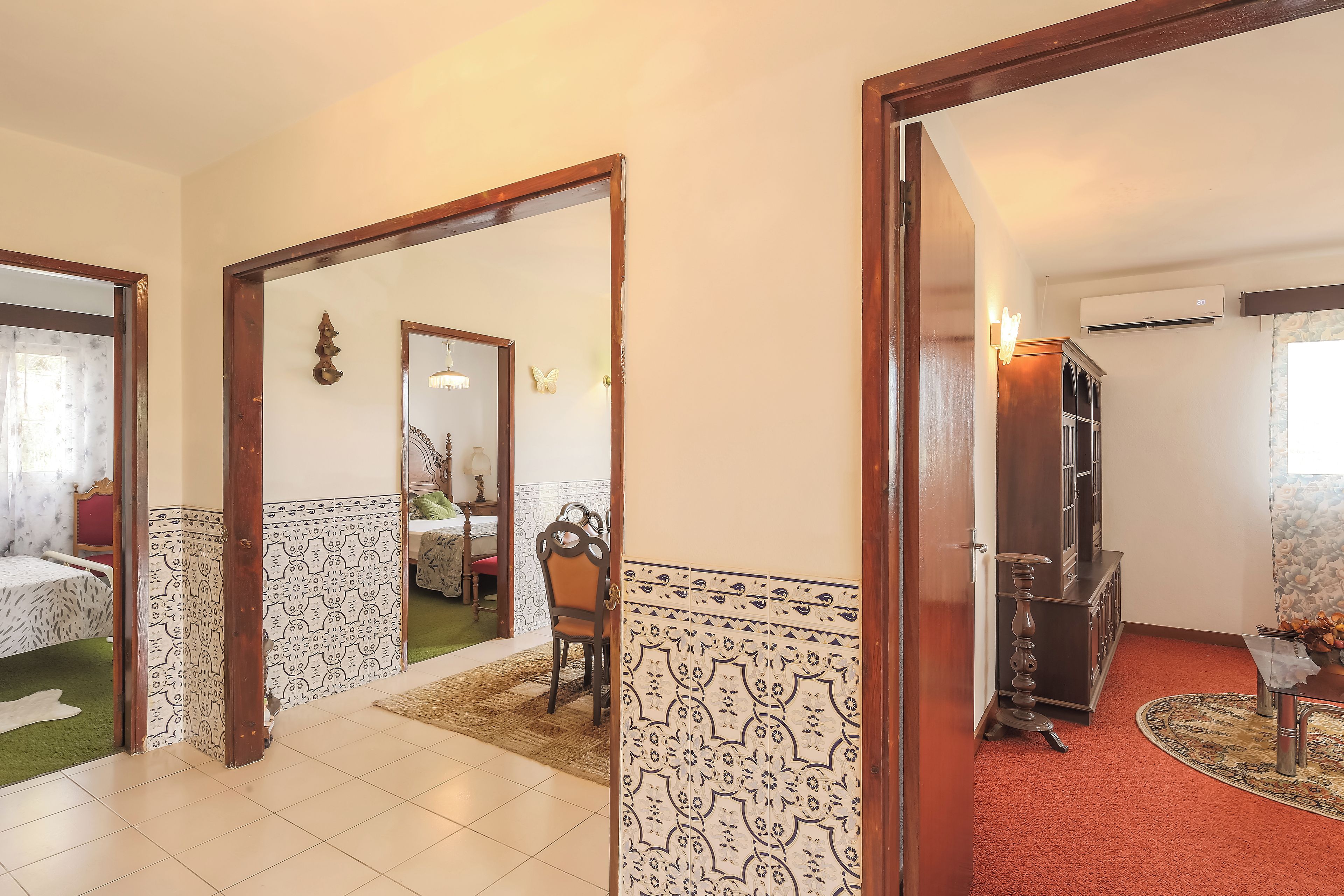 A hallway with a tiled floor, a wooden door frame, and a mirror reflecting a room with a bed and a chair.