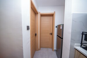 A narrow hallway with a wooden door and a refrigerator on the right. - Cozy&stlyish  1-bedroom apartment in Riara One Residency Lavington Nairobi (Nairobi)