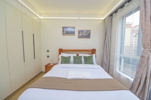 A hotel room with a bed, a nightstand, a wardrobe, and a window with curtains. - Cozy&stlyish  1-bedroom apartment in Riara One Residency Lavington Nairobi (Nairobi)