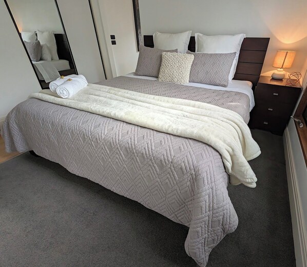 Un lit bien fait, avec une couvre-lit matelassée et des oreillers, une lampe de chevet et un miroir qui reflète la pièce.