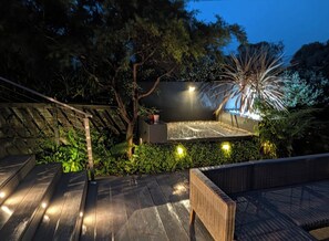 Una terraza en la azotea con un área de estar, un pequeño escenario y un fondo de árboles y follaje.