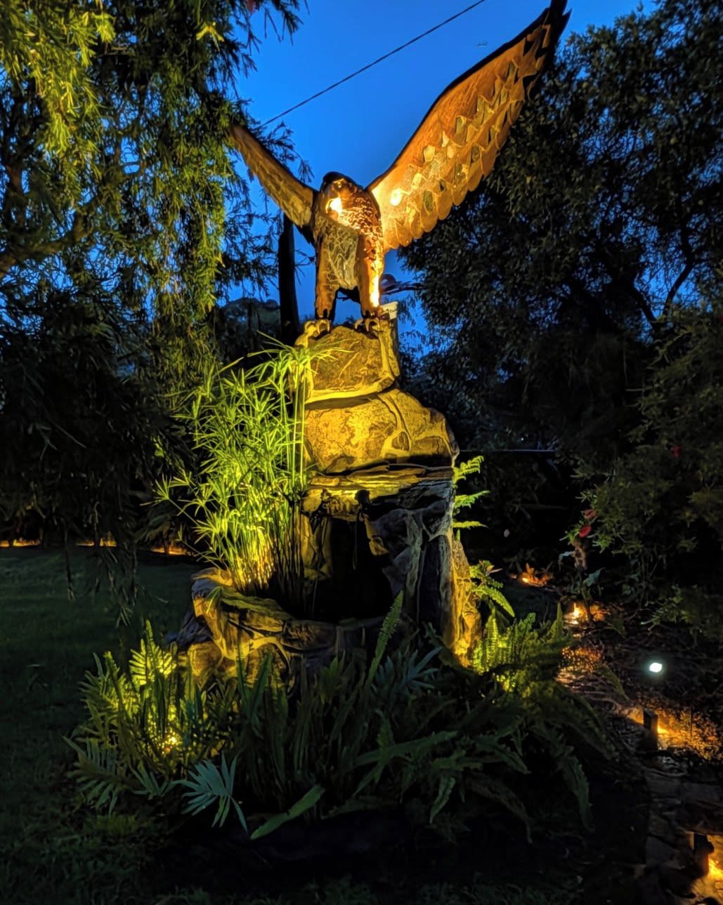 Une sculpture d’oiseau posée sur un rocher, entourée de végétation.