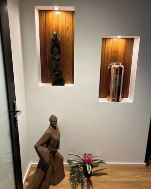 Ein Zimmer mit einer Holzstatue, einem hohen Glasgefäß und einer Topfpflanze.