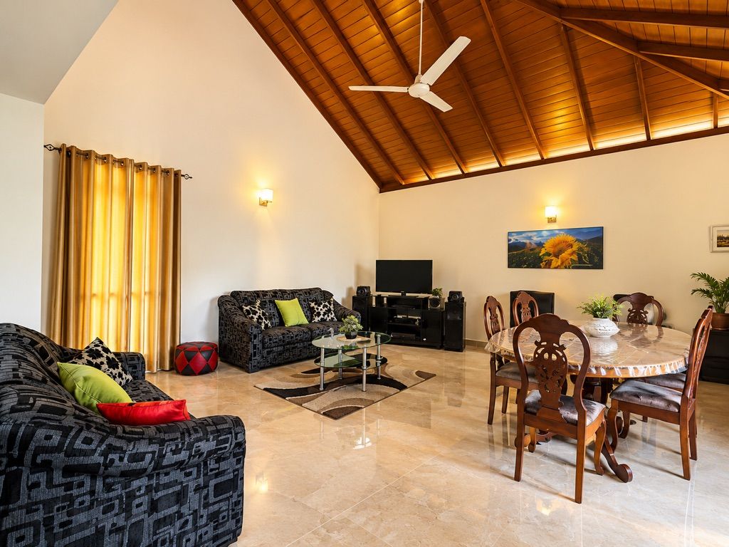 Ampla sala de estar com pé direito alto, ventilador de teto, TV de tela plana, mesa de jantar com cadeiras e sofá com estampa.