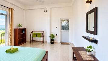 Habitación de hotel con cama, escritorio, silla, ventilador de techo, planta en maceta, estante con espejo y vista al exterior.