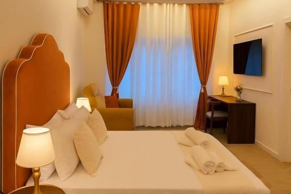 Habitació d'hotel amb llit, làmpada de nit, cortines, televisió i escriptori.