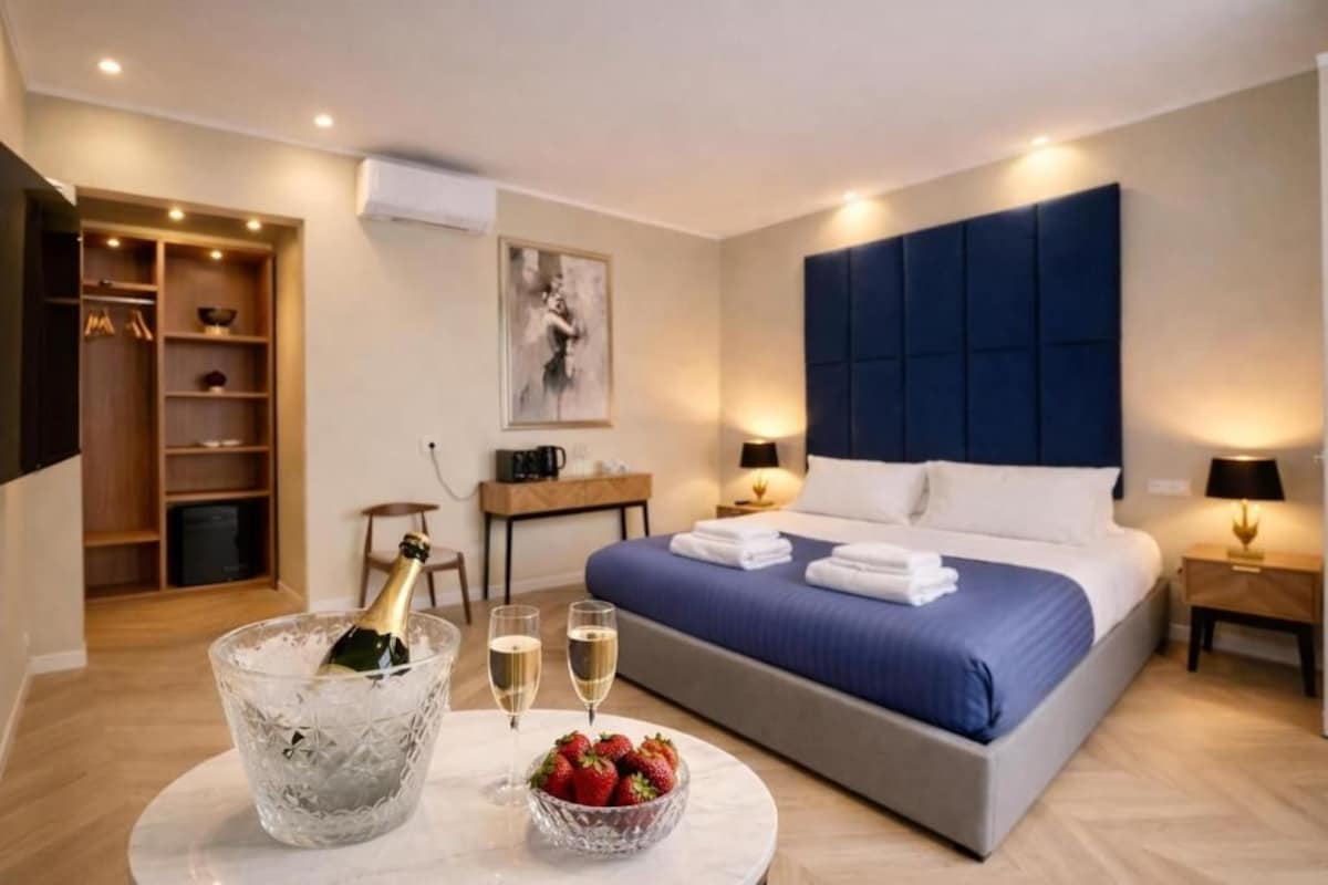 Habitació d'hotel amb llit, taules de nit, barra minibar, armari i un quadre a la paret.