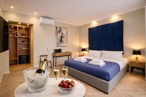 Habitació d'hotel amb llit, taules de nit, barra minibar, armari i un quadre a la paret.