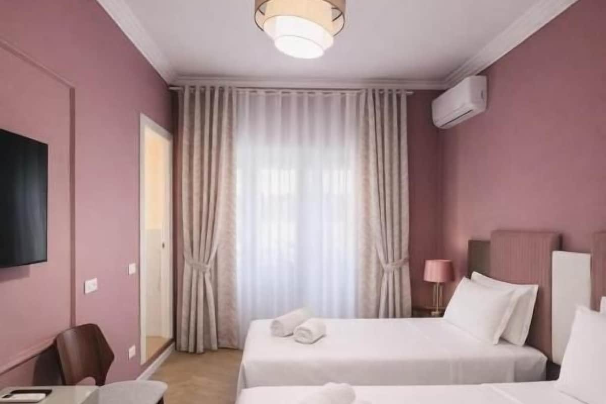 Habitació d'hotel amb dos llits, una taula de treball, una cadira, un televisor i una finestra amb cortines.
