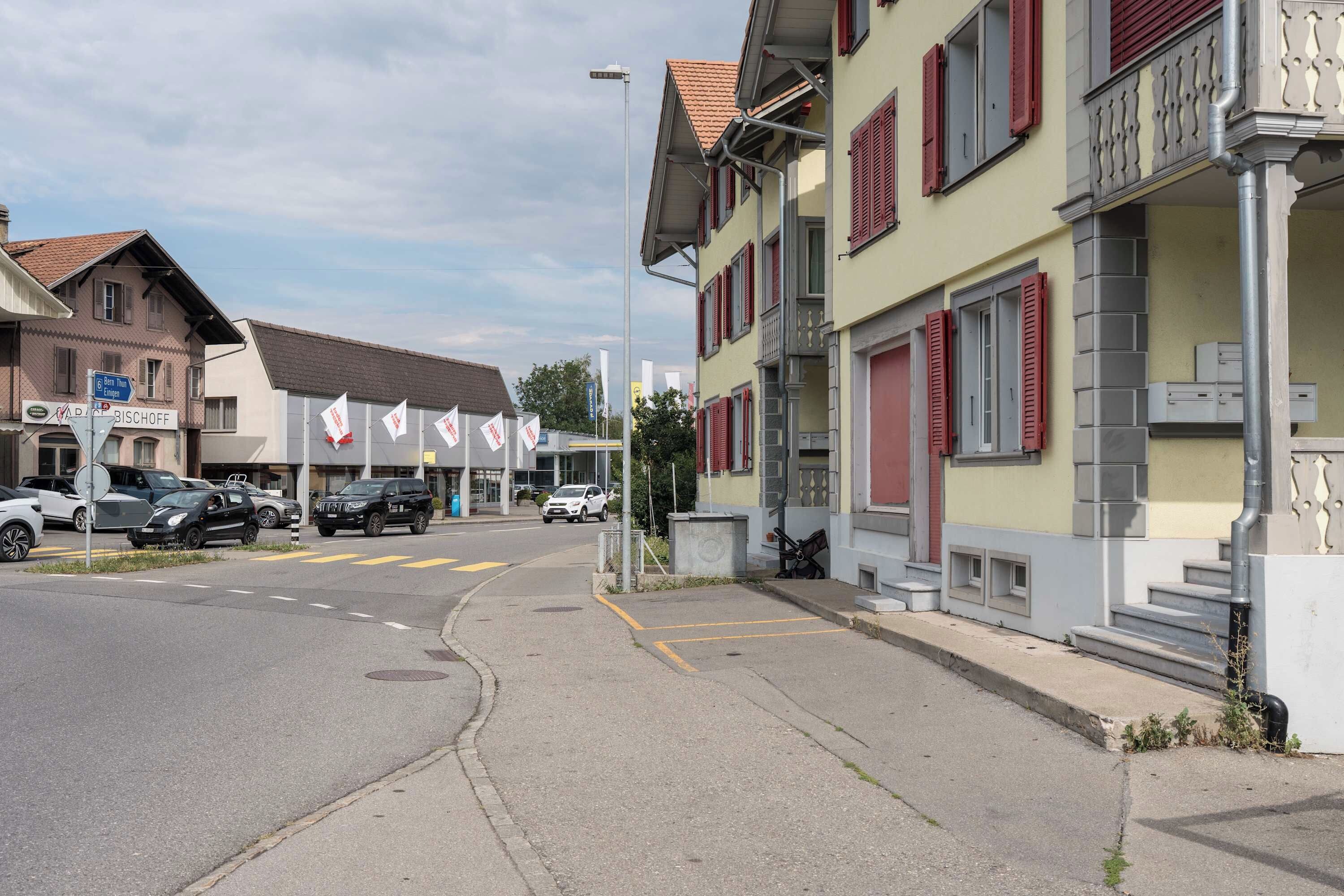 A street with parked cars and a building with red shutters.