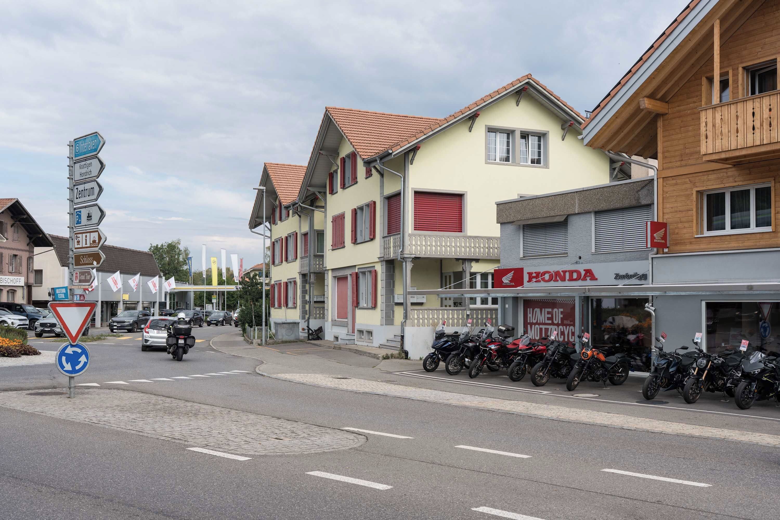 Eine Straße mit Gebäuden, einem Honda-Motorradgeschäft und einem Kreisverkehrschild.