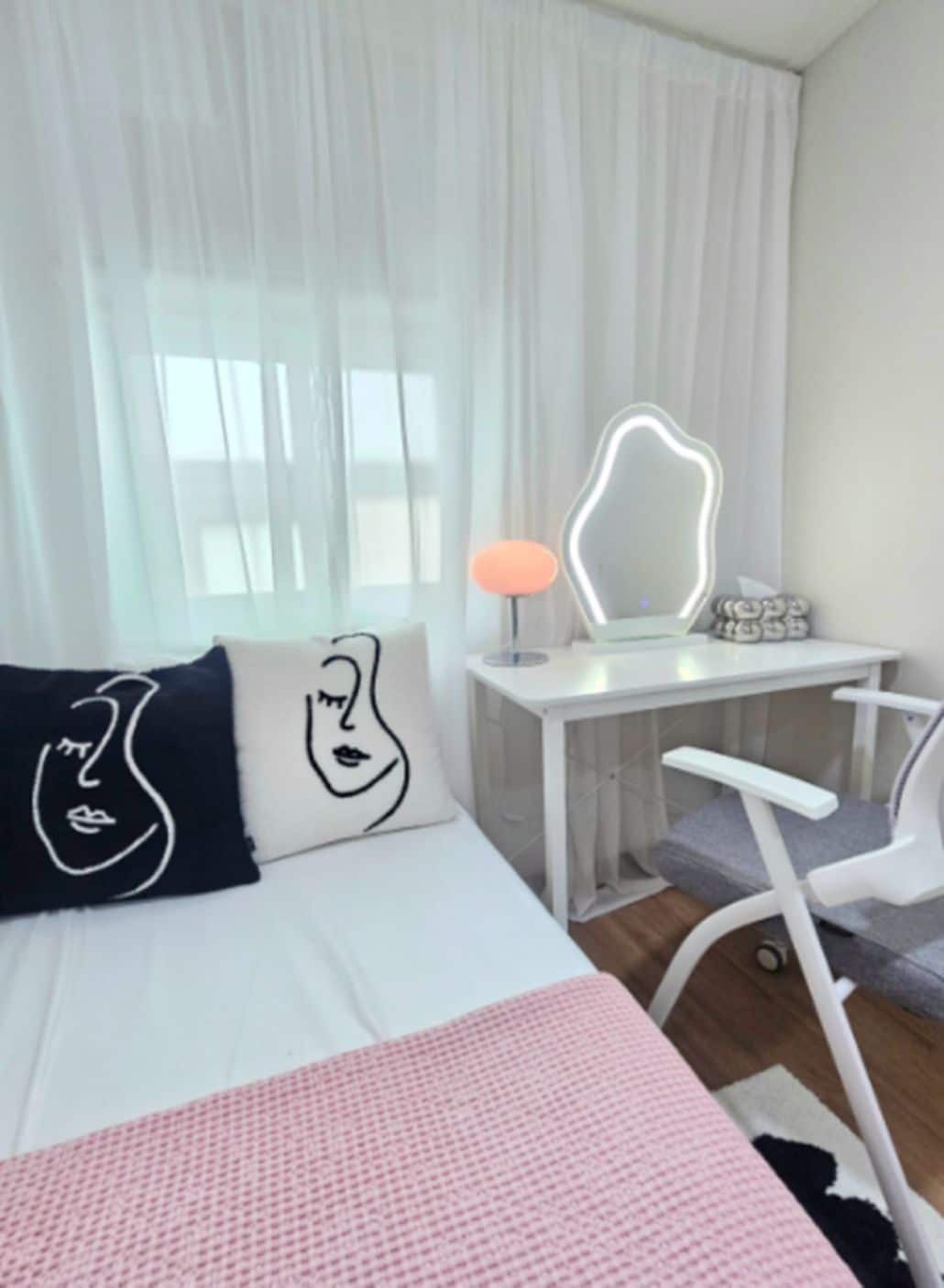 A hotel room with a bed, a desk, a chair, and a large window with sheer curtains.
