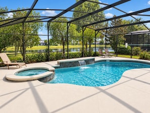 A swimming pool with a waterfall feature, surrounded by lounge chairs and a covered area with a view of a lake and trees. - Private Pool Near Disney with Game Room (Kissimmee)