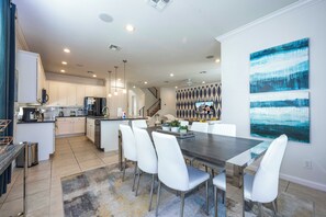A modern kitchen with white cabinets, a black refrigerator, and a dining area with a dark wooden table and white chairs. - Private Pool Near Disney with Game Room (Kissimmee)