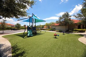 A playground with a blue shade sail, green slides, and a small climbing structure. - Private Pool Near Disney with Game Room (Kissimmee)