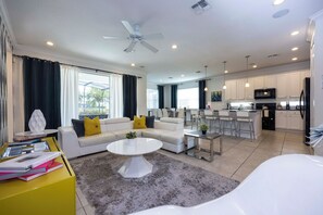 A modern living room with a sofa, coffee table, and a dining area with chairs. - Private Pool Near Disney with Game Room (Kissimmee)