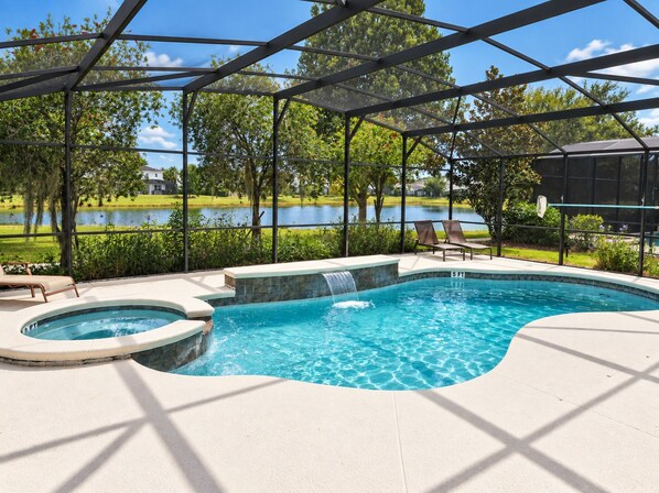 A swimming pool with a waterfall feature, surrounded by a covered area with lounge chairs. - Bella Vida 5BR Pool Home with Game Room & Loft (Kissimmee)
