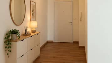 Een hal met houten vloer, een witte deur, een spiegel, een lamp en een lijst met een afbeelding aan de muur.