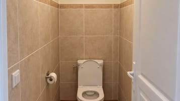 Ein kleines, schmales Badezimmer mit Toilette, einer Toilettenpapierrolle und einer Deckenleuchte.
