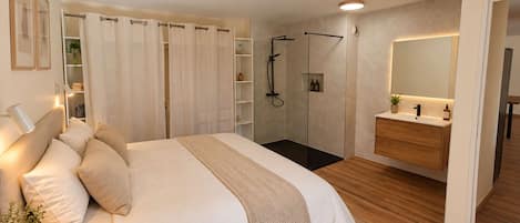 Un dormitorio moderno con una cama grande, un vestidor, zona de ducha y un baño con espejo.