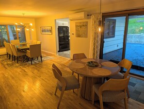 Un coin repas avec une table ronde et des chaises, une cuisine en arrière-plan et une vue sur l’extérieur grâce à une porte vitrée.