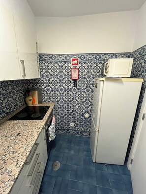 A small kitchen with a microwave on top of a white refrigerator, a sink with a faucet, and a patterned backsplash. - Edifício Corte Real, Albufeira (Albufeira)