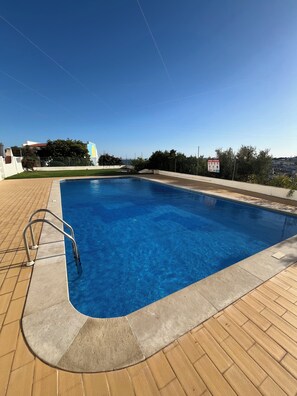 A rectangular swimming pool with a metal ladder on the left side, surrounded by a tiled deck. - Edifício Corte Real, Albufeira (Albufeira)