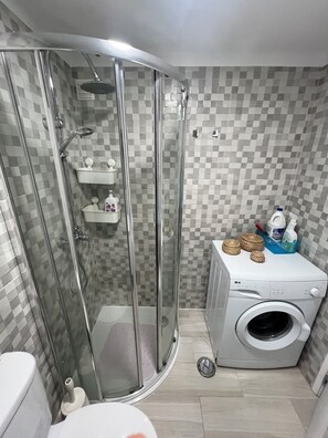 Ein Badezimmer mit einer Duschkabine, einer Waschmaschine und einer gefliesten Rückwand.