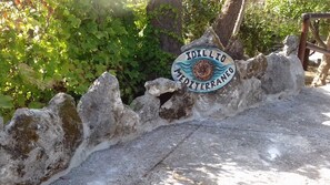 A stone wall with a sign that reads 'IDILLO MERITERRA' and a wooden bench. - Mediterranean Idyll (Sardegna)